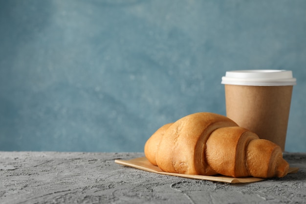 Taza de papel de café y croissant en mesa gris, espacio para texto