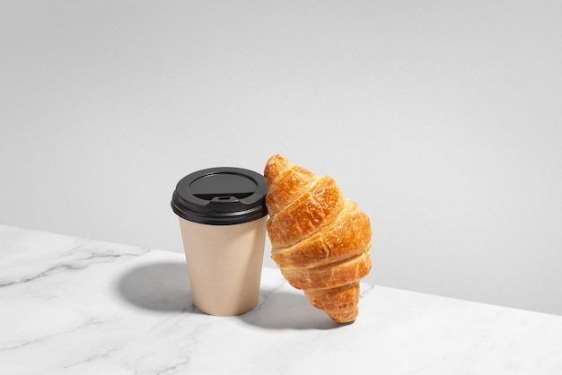 Taza de papel de café con croissant sobre fondo blanco.