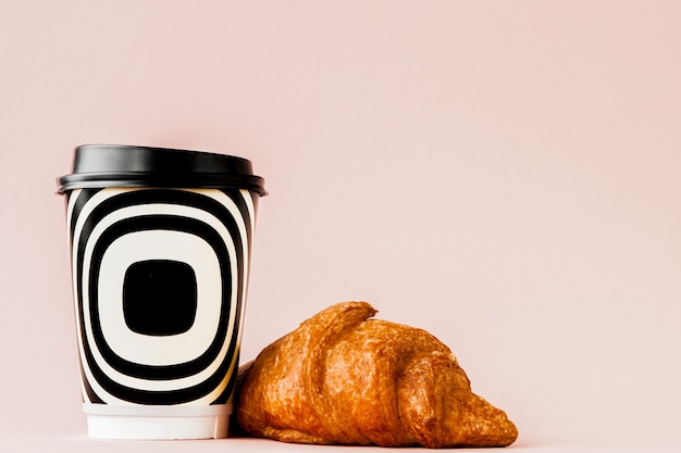 Taza de papel de café y croissants en una pared rosa, espacio de copia.