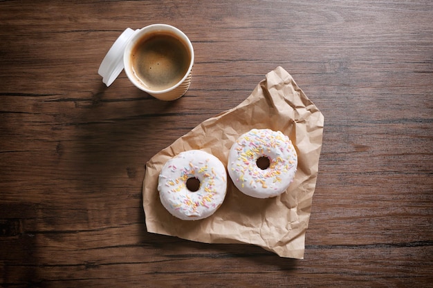 Taza de papel de café y donuts sobre fondo de madera