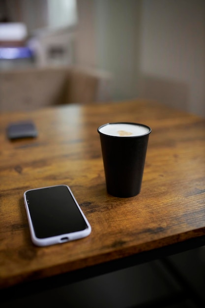 taza de papel de café y teléfono móvil en una mesa de madera marrón, primer plano.