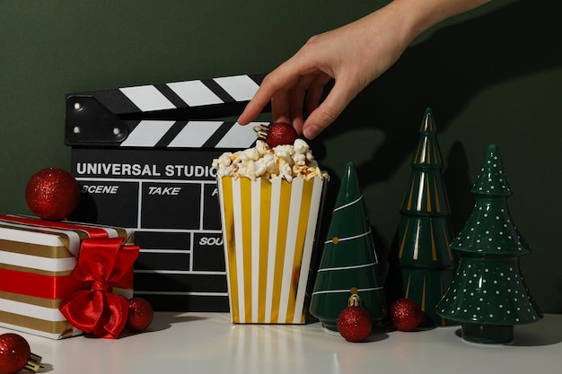 Taza de papel de clapperboard con mano de palomitas de maíz y decoraciones navideñas en fondo verde