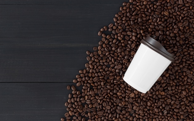 Taza de papel y grano de café en fondo de madera negro. vista superior