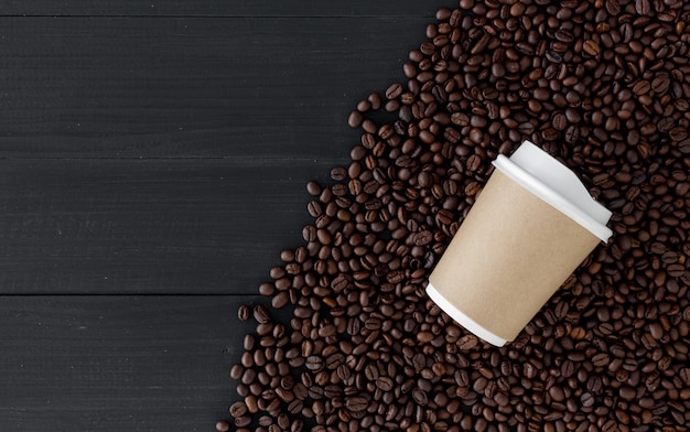 Taza de papel y grano de café en fondo de madera negro. vista superior