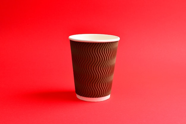 Taza de papel marrón sobre un fondo rojo.