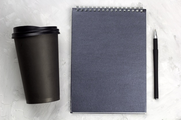 Taza de papel negra de café para llevar cuaderno y bolígrafo negro