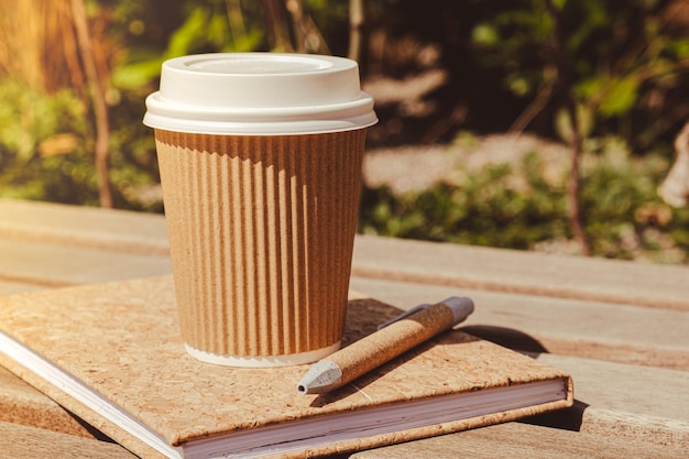 Foto taza de papel de reciclaje ecológico con café o té en papel kraft con cuaderno de papel vacío en un banco de madera