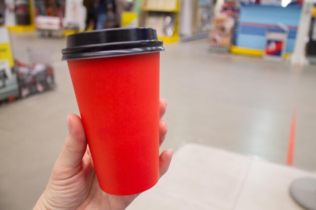 Una taza de papel roja con café o té en manos de una chica