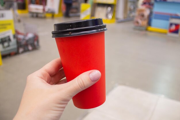 Una taza de papel roja con café o té en manos de una niña. Una maqueta.