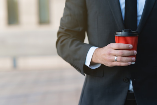 La taza de papel roja con café en varón da el primer. Hombre de negocios en un traje