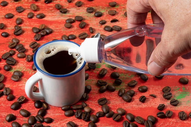 Foto taza pequeña de café con frijoles en el lateral y mesa rústica roja endulzada