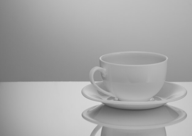 Una taza y un platillo blancos sobre un fondo claro con reflejo