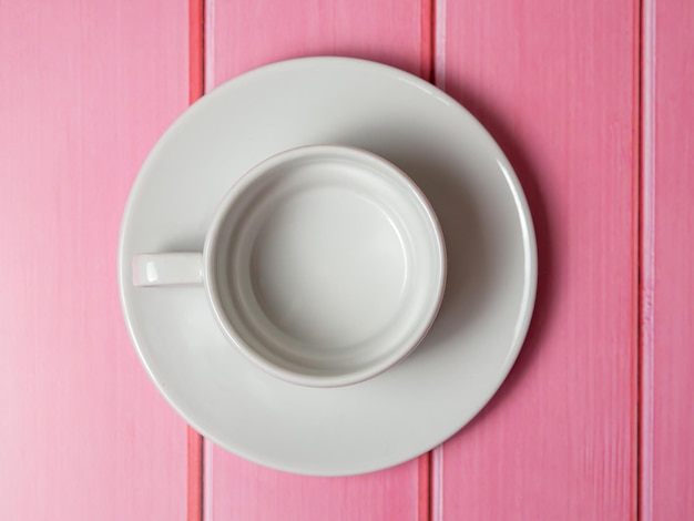 Taza y plato blanco vacío sobre una mesa de madera rosa