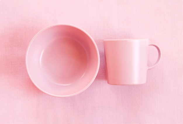 Taza y plato de color rosa sobre una superficie de tela rosa suave