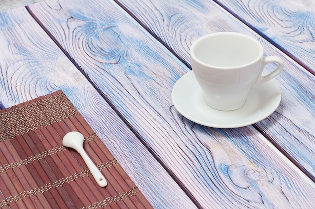 Taza de porcelana blanca con platillo y una cuchara de té sobre una servilleta de bambú con el fondo de madera.