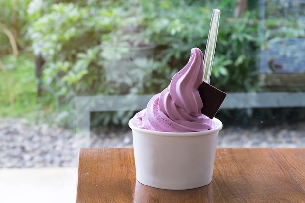 Una taza de Purple Sweet potato soft serve o helado en la mesa de madera con desenfoque de fondo de árbol verde