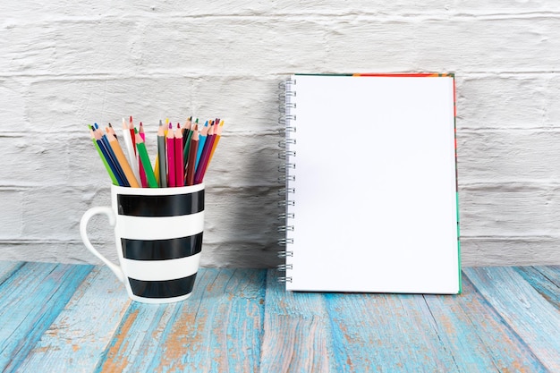 Taza a rayas llena de lápices de colores y un bloc de notas sobre un bonito fondo con espacio para copiar