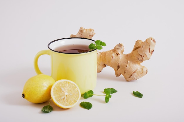 Taza de rea, raíz de jengibre, hojas de menta y limones sobre un fondo gris, beneficios para la salud del jengibre, bebida natural para el espacio de copia de inmunidad