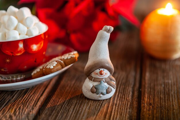 Taza roja con bebida caliente y malvavisco con pan de jengibre. Concepto de Navidad con flor de nochebuena, vela encendida y decoración navideña. Primer plano, enfoque selectivo, poca profundidad de campo.