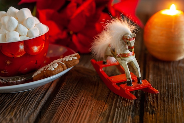 Taza roja con bebida caliente y malvavisco con pan de jengibre. Concepto de Navidad con flor de nochebuena, vela encendida y decoración navideña. Primer plano, enfoque selectivo, poca profundidad de campo.