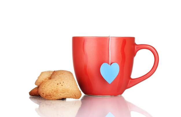 Taza roja con bolsita de té y galletas en forma de corazón aislado en blanco