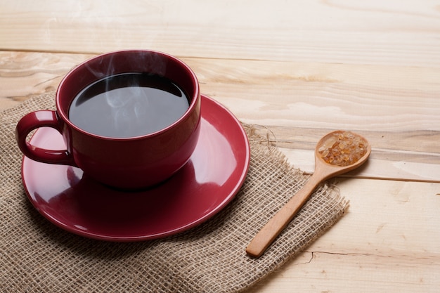 Taza roja de café y azúcar en cuchara sobre arpillera en fondo de madera