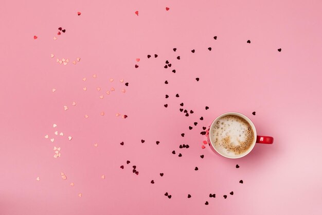 Taza roja de café con crema y confeti caótico en forma de corazón San Valentín