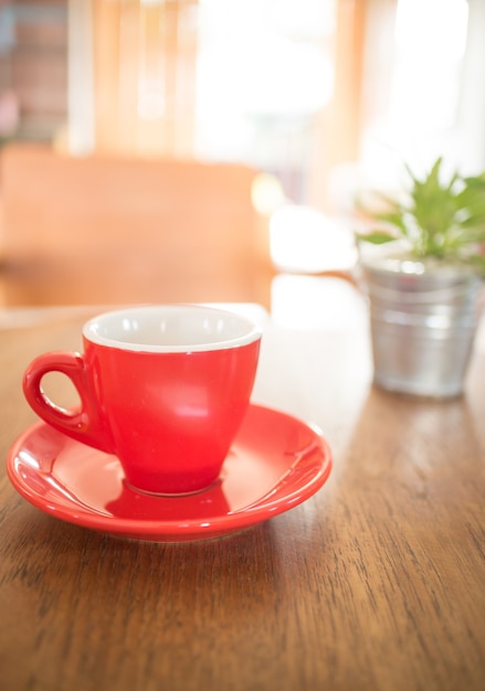 Taza roja de café y cubo de planta verde en mesa de madera