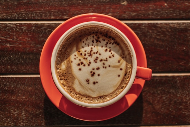 Taza roja de café con leche caliente en la mesa de madera temprano en la mañana.