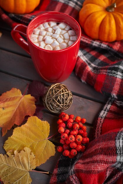 Taza roja con café y malvaviscos. Estado de ánimo de otoño, bebida caliente. Ambiente acogedor, calabazas amarillas.