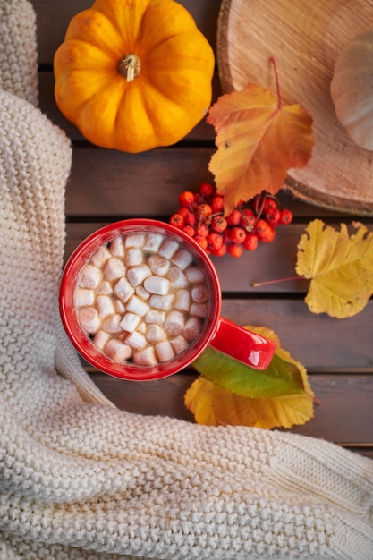 Taza roja con café y malvaviscos. Estado de ánimo de otoño, bebida caliente. Ambiente acogedor, calabazas amarillas.