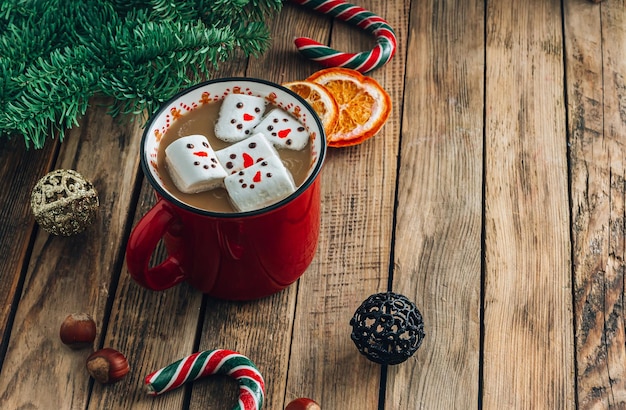 Taza roja con capuchino con muñecos de nieve de malvaviscos derretidos sobre fondo de madera festivo Enfoque selectivo con espacio de copia