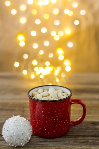 Taza roja de chocolate caliente con bolas blancas de malvaviscos y bastones de caramelo. fondo con hermosas luces de Navidad bokeh.