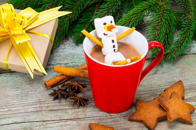 Taza roja con chocolate caliente con muñeco de nieve de malvavisco derretido.