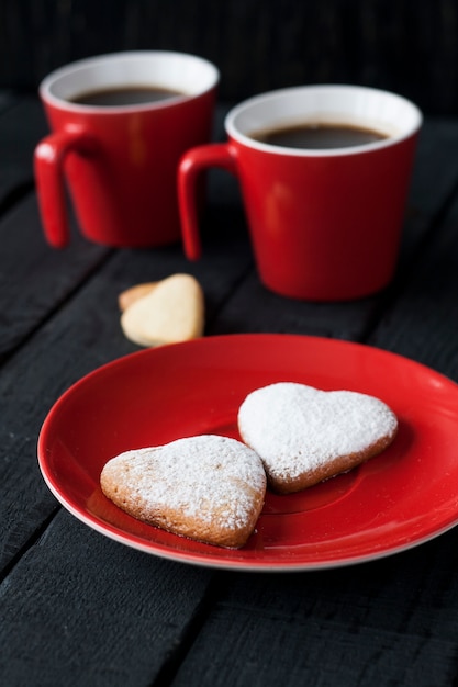 Taza roja y corazones de galletas en una superficie negra para el día de San Valentín