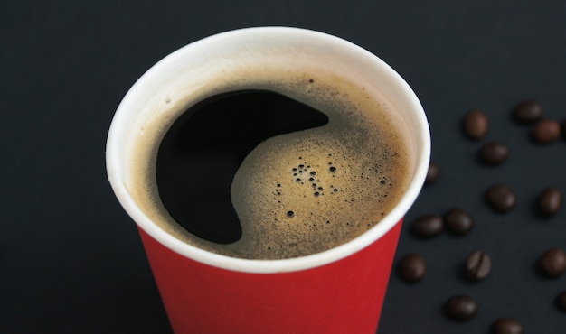 Taza roja desechable con café negro caliente recién hecho y granos tostados sobre un fondo negro El concepto de café para llevar