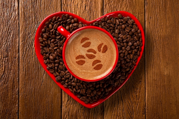 Taza roja y platillo de café en forma de corazón con café decorado en espacio de madera vieja. Vista superior. forma de grano en el café.