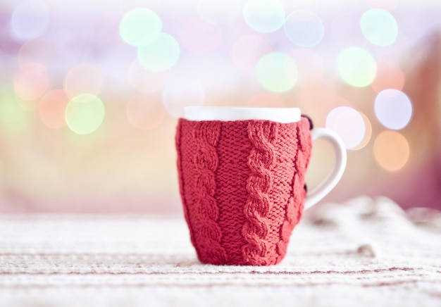 Taza roja tejida con luces navideñas en el fondo