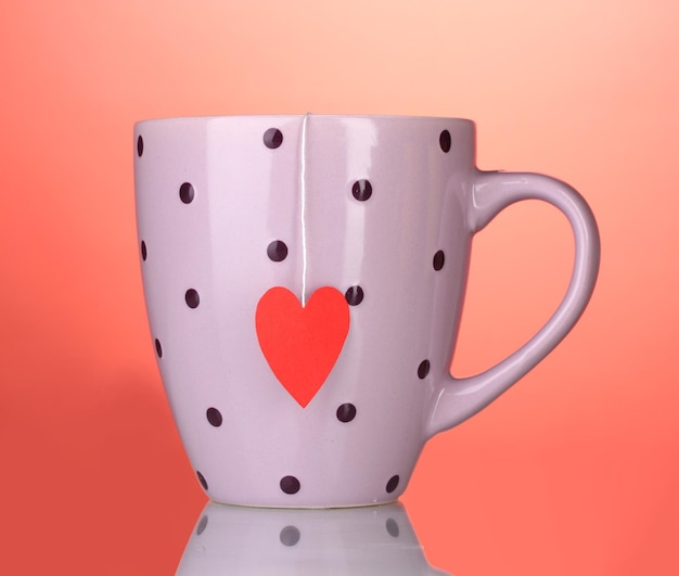 Taza rosa y bolsita de té con etiqueta roja en forma de corazón sobre fondo rojo.