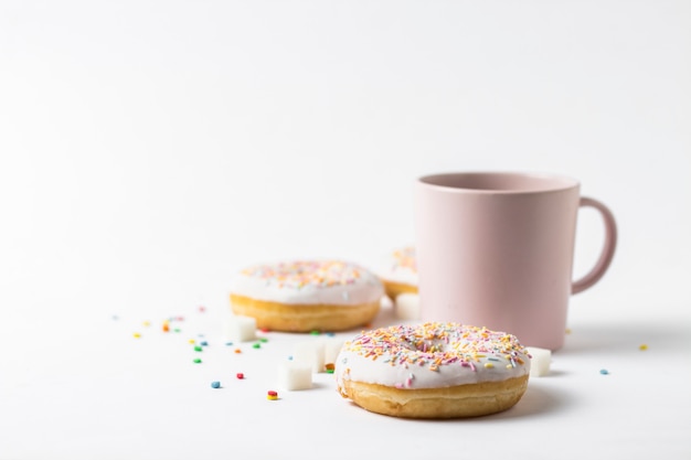 Taza rosa con café o té y donuts sabrosos frescos, dulce dulce decorativo multicolor sobre un fondo blanco. Concepto de panadería, pasteles frescos, delicioso desayuno, comida rápida.