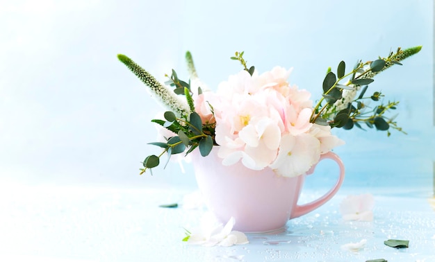 Una taza rosa llena de flores Hydrangea veronica eucolyptus ramitas