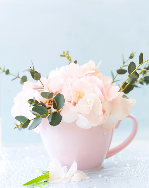 Una taza rosa llena de flores Hydrangea veronica ramitas de eucalipto