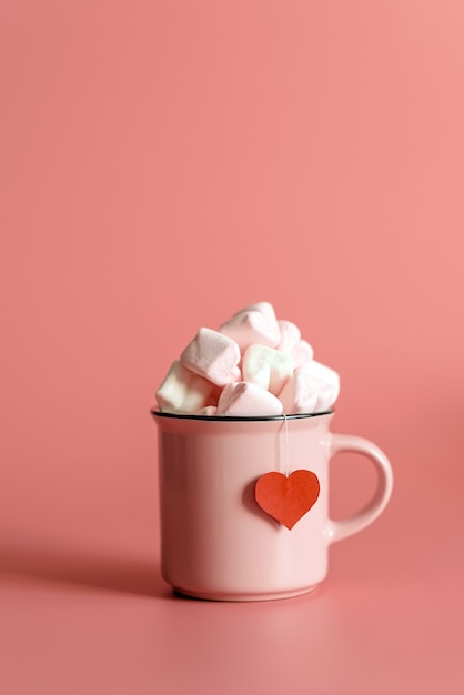 Taza rosa llena de malvaviscos en forma de corazones