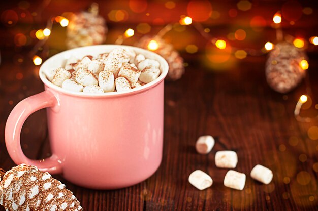 Taza rosa con malvaviscos sobre un fondo de madera Guirnalda de Navidad y juguetes en el fondo