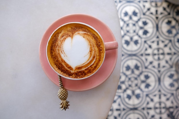 Taza rosa de moda de capuchino caliente sobre fondo de mesa de mármol Arte latte en forma de corazón para símbolo de amor Una taza para la rutina matutina