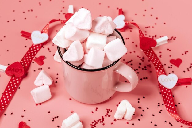 Taza rosa sobre fondo rosa llena de malvaviscos en forma de corazones. concepto de vacaciones del día de san valentín