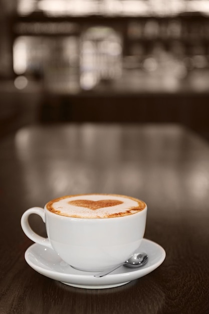 Taza con sabroso café caliente en la mesa de madera en la cafetería vista de cerca