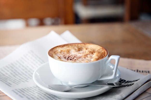 Taza de sabroso capuchino y periódicos en la mesa