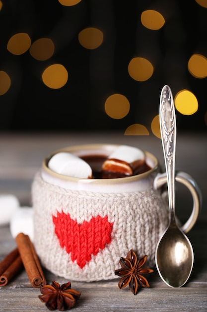 Taza de sabroso chocolate caliente, sobre mesa de madera, sobre fondo brillante