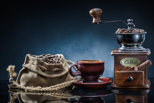 Taza y saco de molinillo de café con frijoles en la mesa del espejo